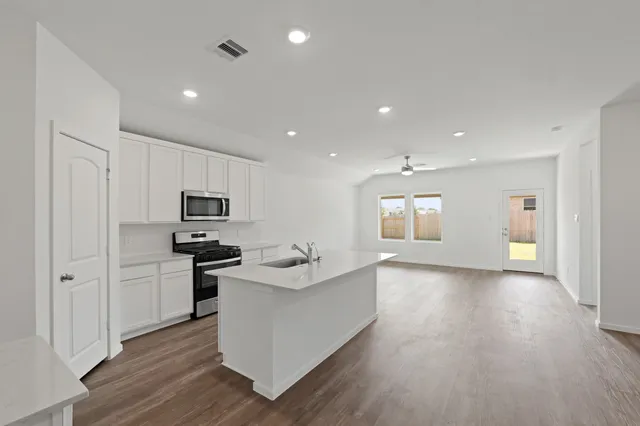 a living room with stainless steel appliances kitchen island granite countertop a stove a sink a refrigerator and white cabinets with wooden floor