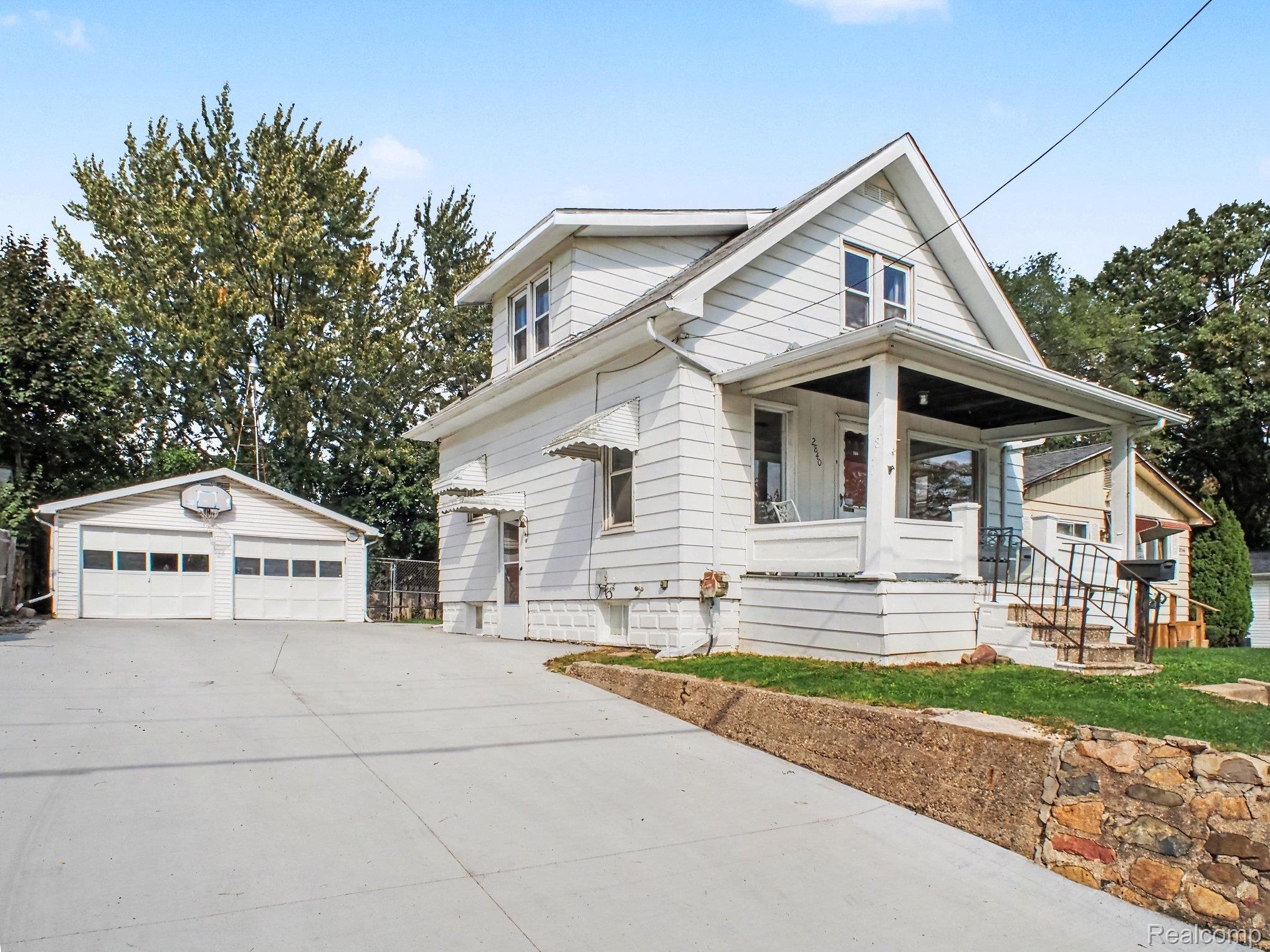 2840 Miller Road Flint, MI 48503 - Photo 1 of 49 White siding exterior with an attached front porch, concrete driveway, two-car detached garage, and stone retaining wall