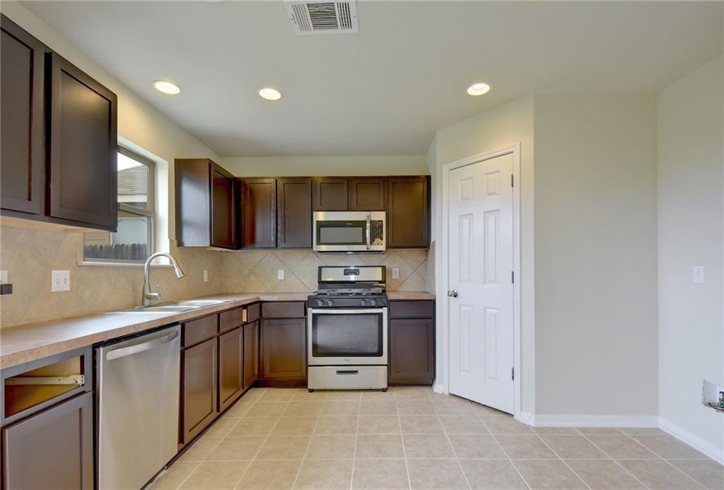 4502 Kind Way Austin, TX 78725 - Photo 12 of 13 Kitchen featuring stainless steel appliances, light countertops, dark wood finish cabinets, recessed lighting, and tasteful backsplash