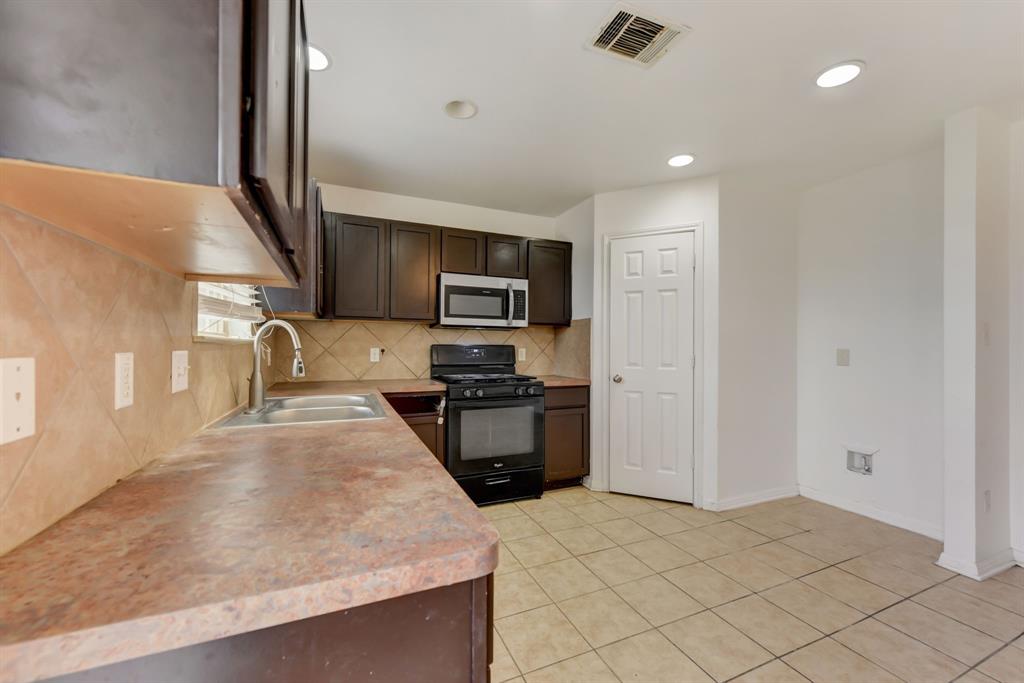 4502 Kind Way Austin, TX 78725 - Photo 13 of 13 Kitchen featuring dark wood finish cabinetry, black range with gas stovetop, stainless steel microwave, light countertops, and tasteful backsplash