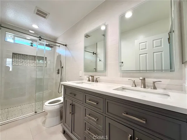 a bathroom with a double vanity sink toilet mirror and shower