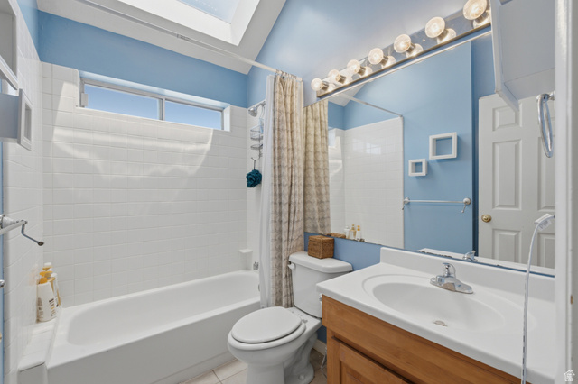 5788 Walden Ridge Drive Murray, UT 84123 - Photo 24 of 29 Bathroom featuring a skylight, white tile shower surround, window above the shower, wood-finish vanity, and a large mirror with integrated lighting