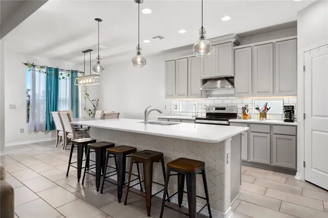 a kitchen with stainless steel appliances kitchen island granite countertop a sink a stove a refrigerator and island with wooden floor