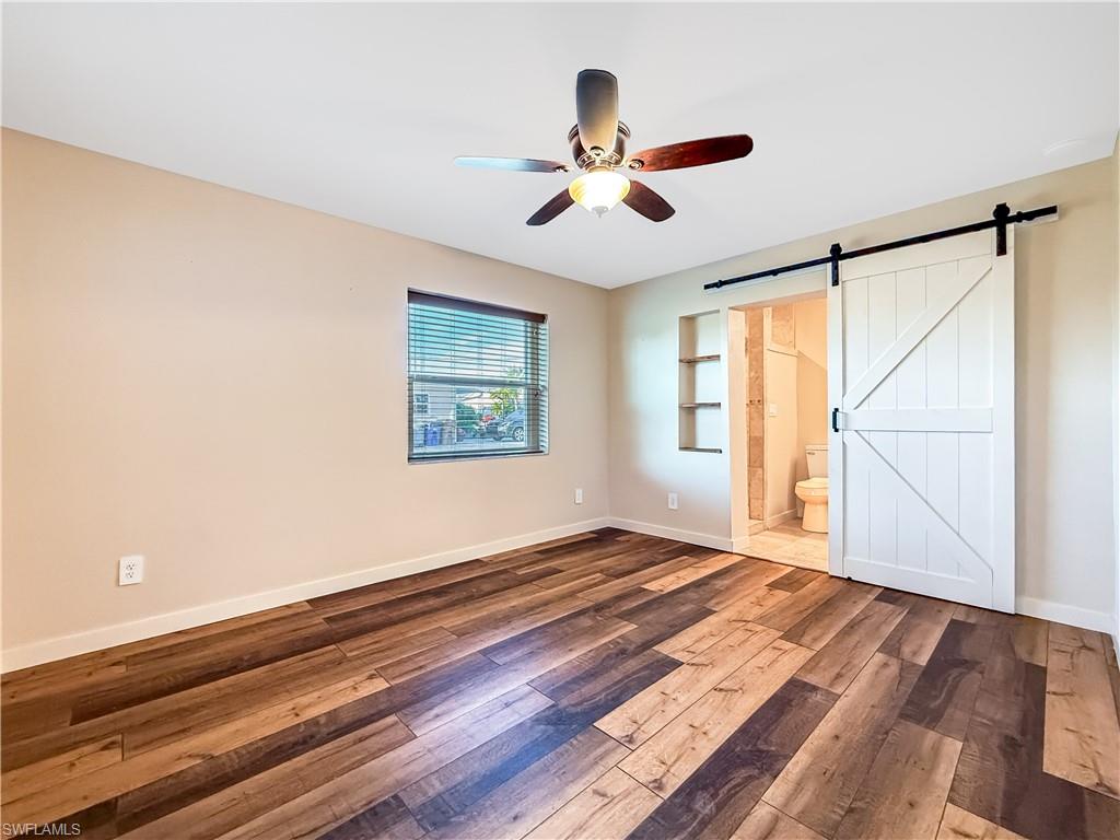 2115 St Croix Avenue Fort Myers, FL 33905 - Photo 15 of 37 Unfurnished bedroom with a barn door, hardwood / wood-style flooring, a ceiling fan, and ensuite bathroom