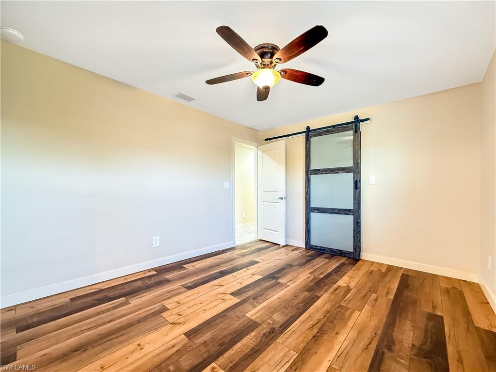 2115 St Croix Avenue Fort Myers, FL 33905 - Photo 16 of 37 Unfurnished bedroom featuring a barn door, hardwood / wood-style flooring, and a ceiling fan