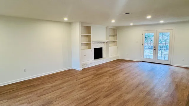 an empty room with wooden floor fireplace and windows