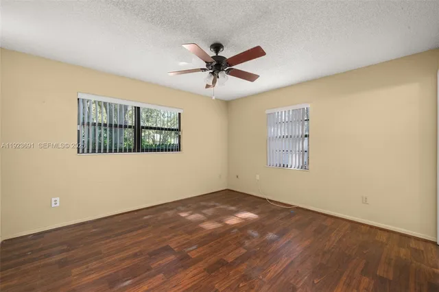 an empty room with wooden floor ceiling fan and windows