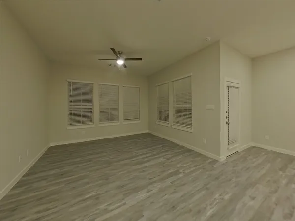 a view of an empty room with wooden floor and a ceiling fan