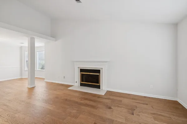 a view of an empty room with wooden floor fireplace and a window