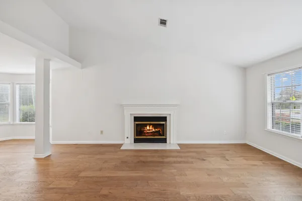 an empty room with wooden floor fireplace and windows