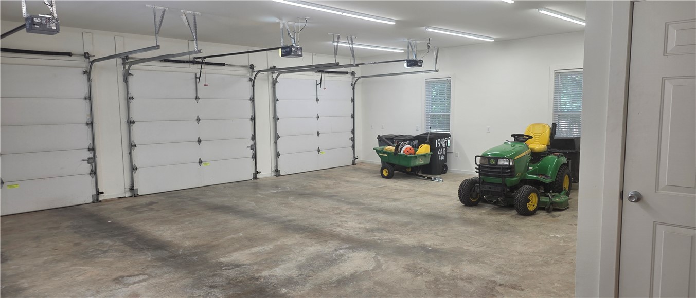 19489 Oak Circle Springdale, AR 72764 - Photo 57 of 58 Spacious three-bay garage with automatic overhead doors, concrete flooring, and multiple ceiling-mounted fluorescent light fixtures