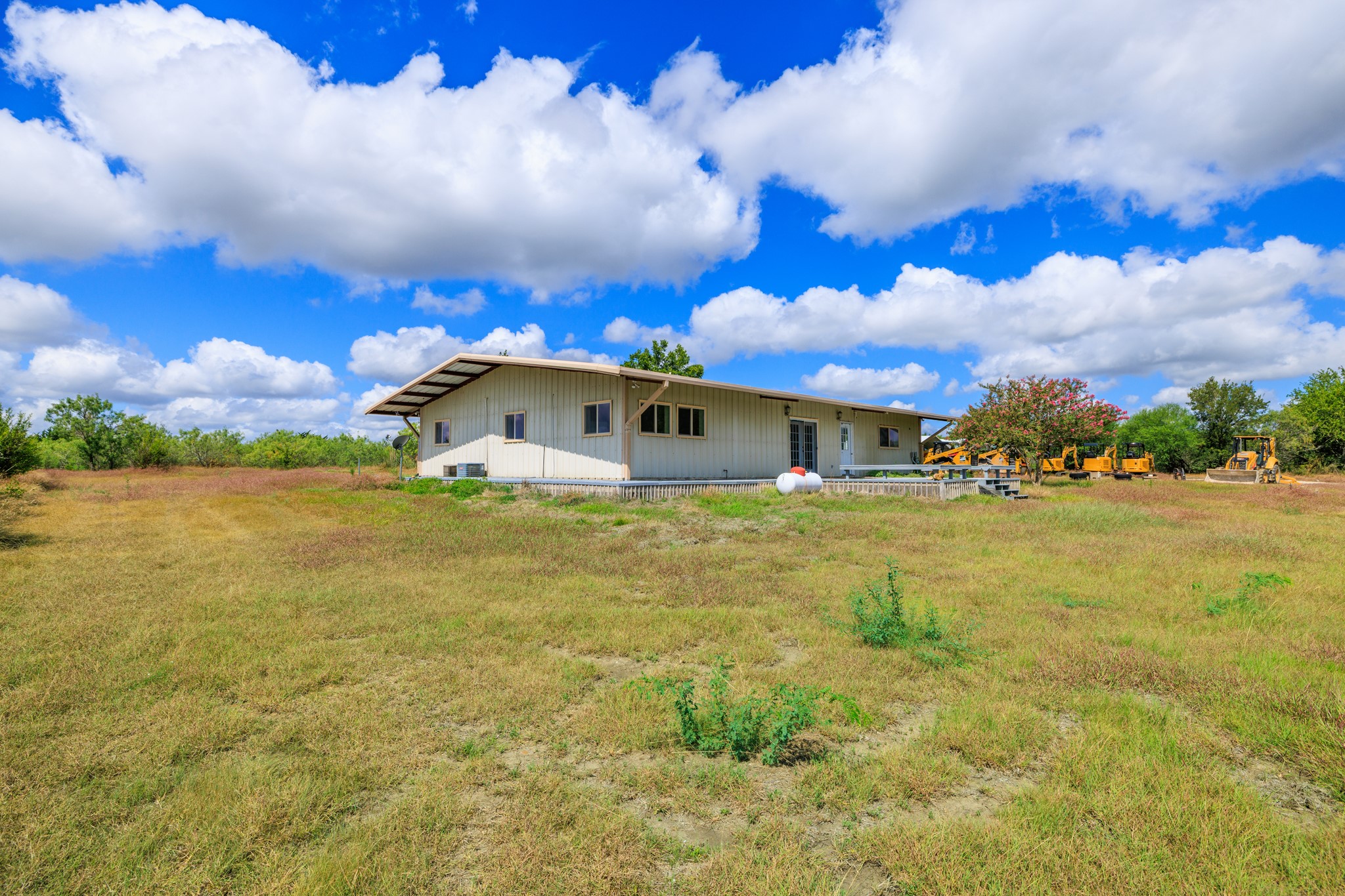 8804 Williamson Road Buda, TX 78610 - Photo 25 of 37 A single-story structure stands set back against a vast grassy clearing under a blue sky.