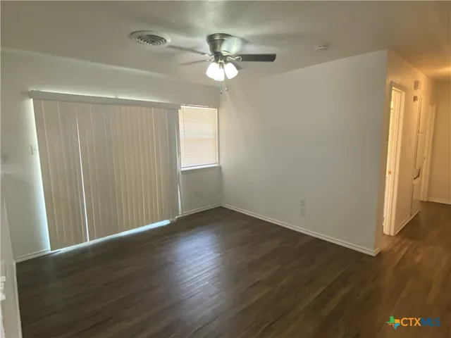 an empty room with wooden floor fan and windows