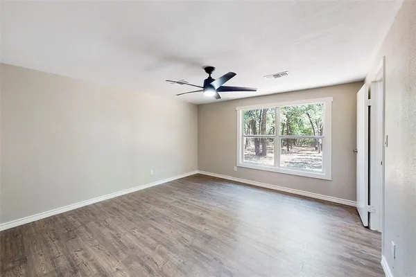 an empty room with wooden floor fan and windows