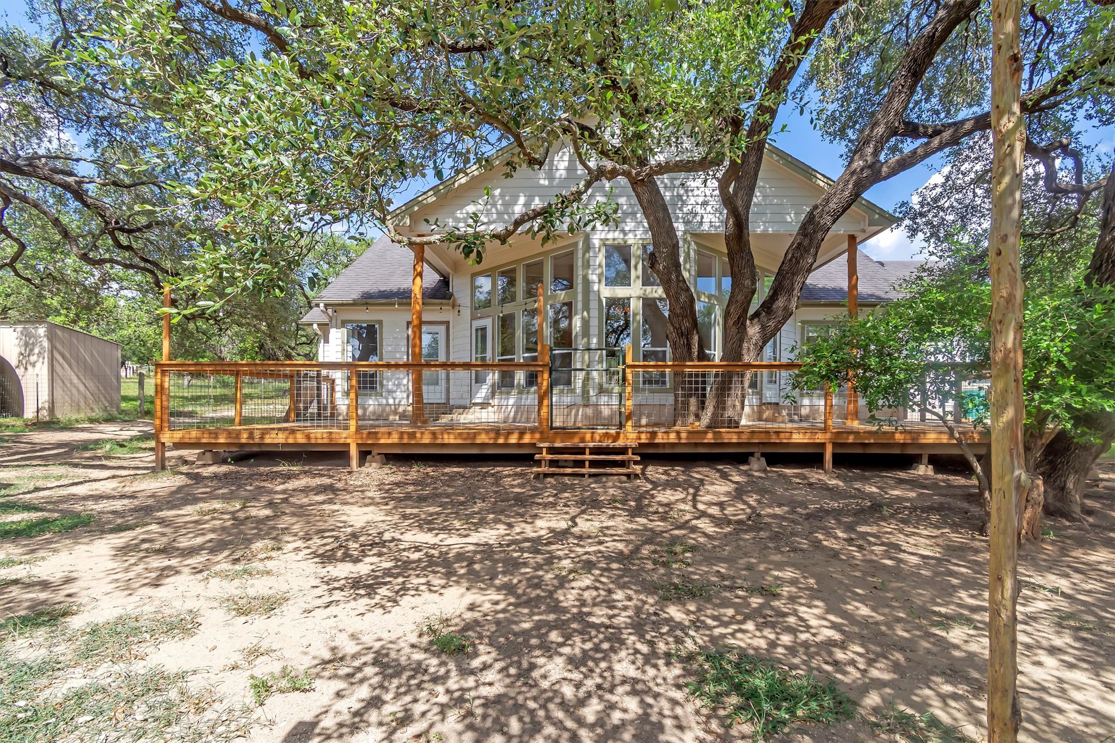 1120 Meadow Ridge Drive Austin, TX 78737 - Photo 27 of 40 A spacious wooden deck extends from the rear, shaded by mature trees with a small storage shed visible nearby.