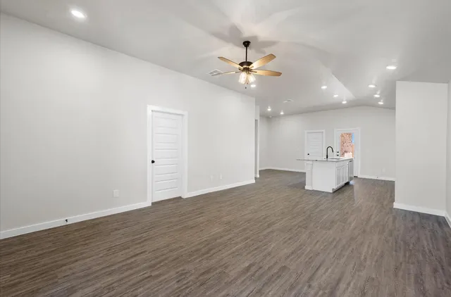 a view of an empty room with wooden floor and a ceiling fan