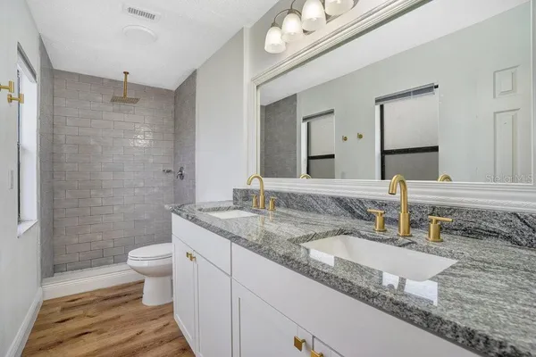 a bathroom with a granite countertop sink a toilet a mirror and shower