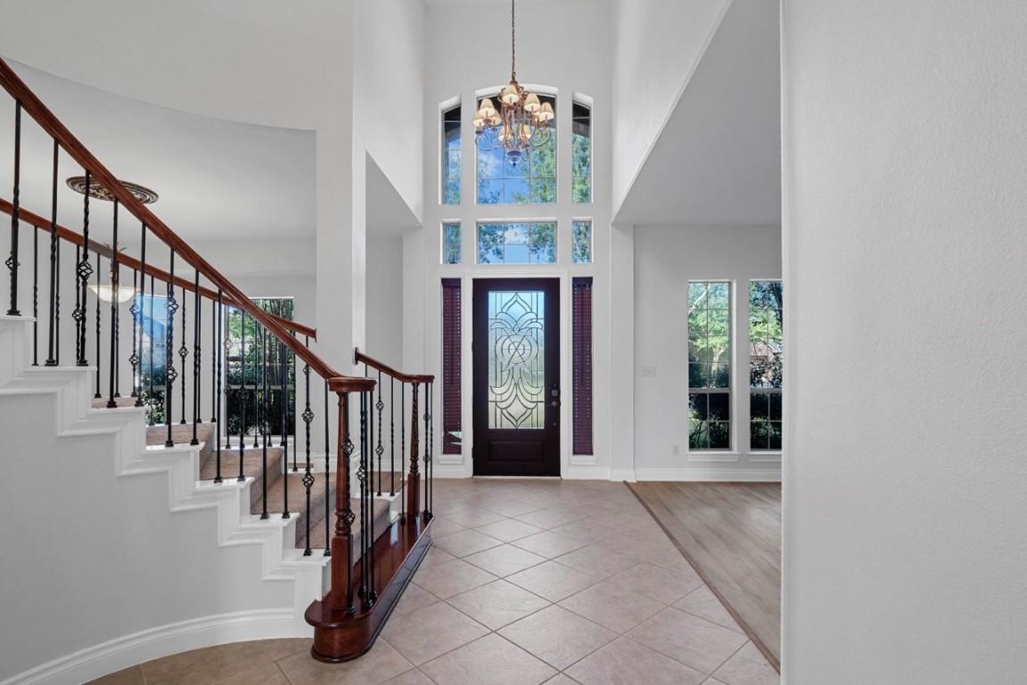 26411 Ridgefield Park Lane Cypress, TX 77433 - Photo 9 of 50 This entryway features a grand staircase with elegant wrought iron railings, high ceilings, and ample natural light from large windows. The front door has decorative glass, and the space transitions smoothly from tile to wood flooring, creating an inviting atmosphere.