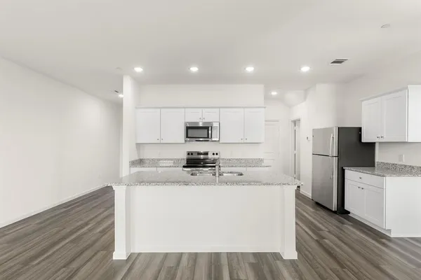 a kitchen with stainless steel appliances a stove top oven a sink a refrigerator white cabinets and wooden floor