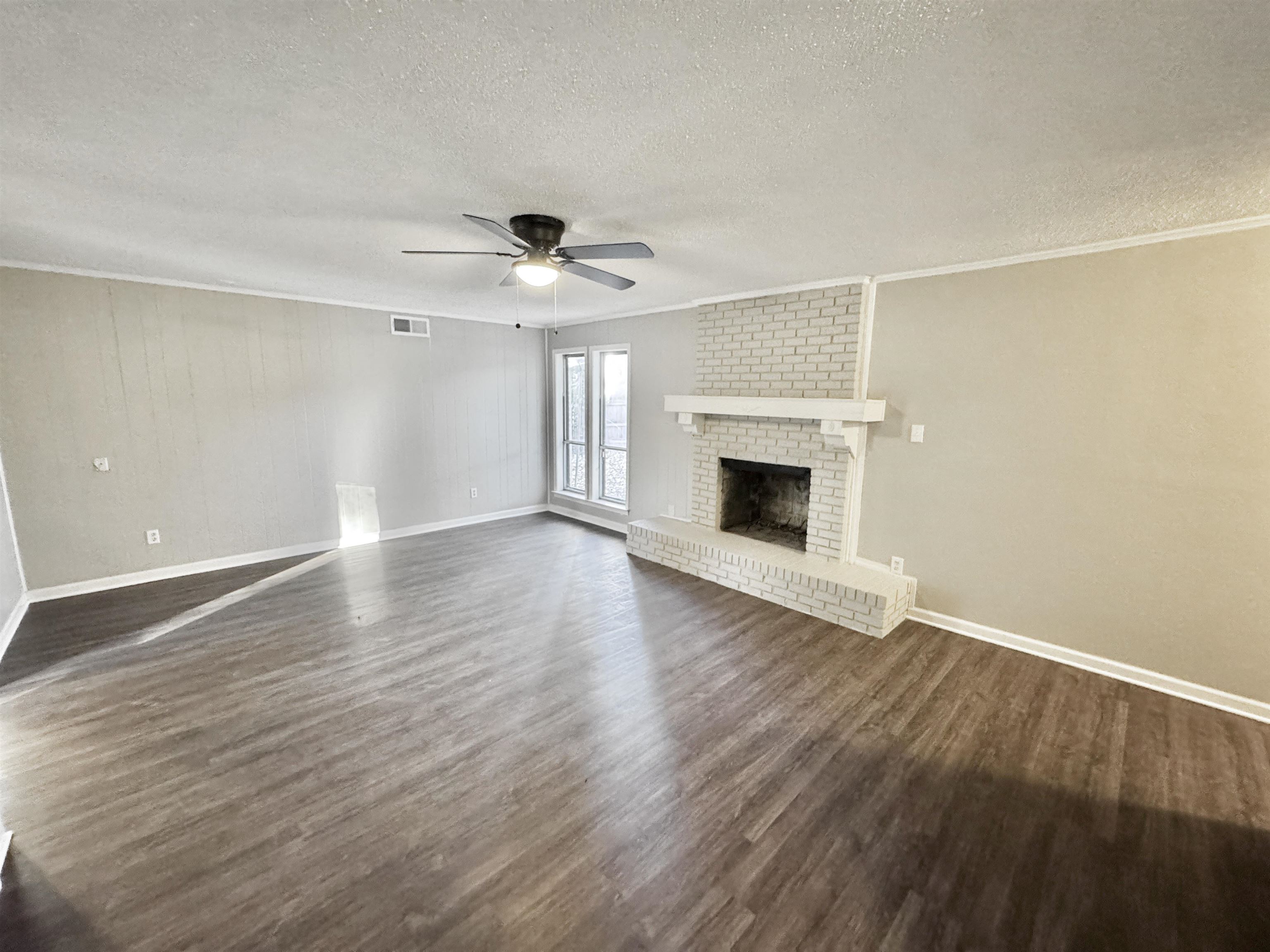 3836 Birchleaf Road Memphis, TN 38116 - Photo 4 of 40 Unfurnished living room with dark wood-style floors, a textured ceiling, a brick fireplace, a ceiling fan, and crown molding
