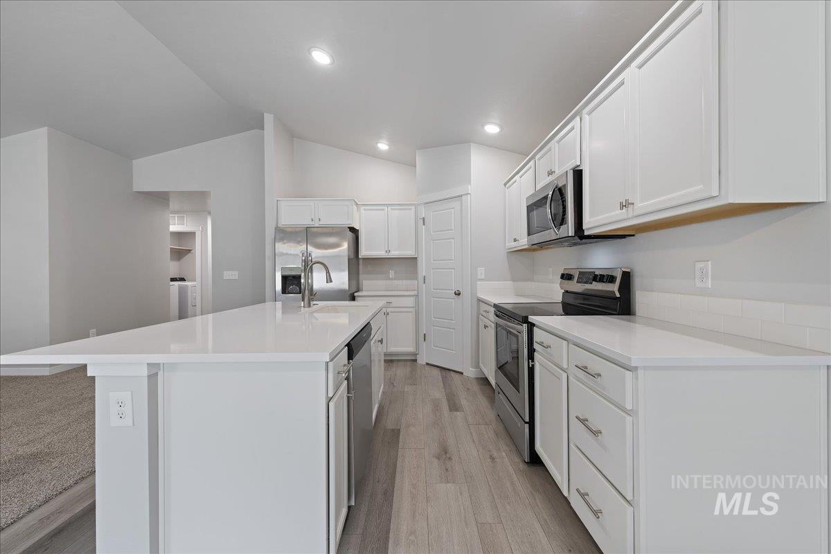 3079 S Green Boise, ID 83709 - Photo 12 of 35 Kitchen with stainless steel appliances, white cabinets, lofted ceiling, light wood-type flooring, and a center island with sink
