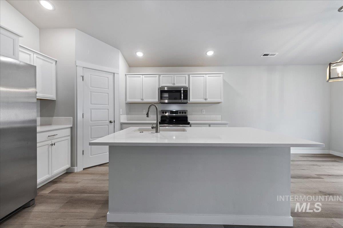 3079 S Green Boise, ID 83709 - Photo 14 of 35 Kitchen with stainless steel appliances, white cabinets, light wood-style floors, and a kitchen island with sink