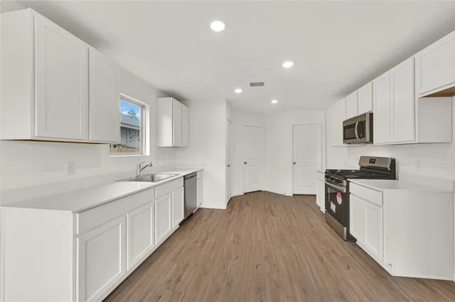 a kitchen with stainless steel appliances a sink dishwasher a stove top oven a refrigerator with white cabinets and wooden floor