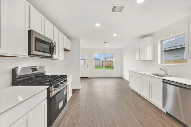 a kitchen with granite countertop a stove top oven a sink dishwasher and white cabinets with wooden floor