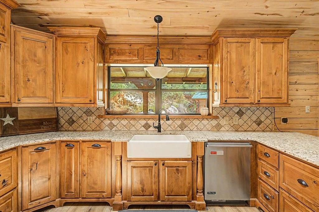 Wood-finish cabinetry, tile backsplash, farmhouse sink with a gooseneck faucet, light-toned countertops, and a built-in stainless steel appliance