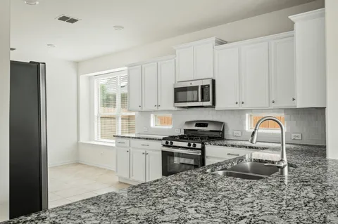 a kitchen with stainless steel appliances granite countertop a stove top oven a sink a refrigerator and white cabinets