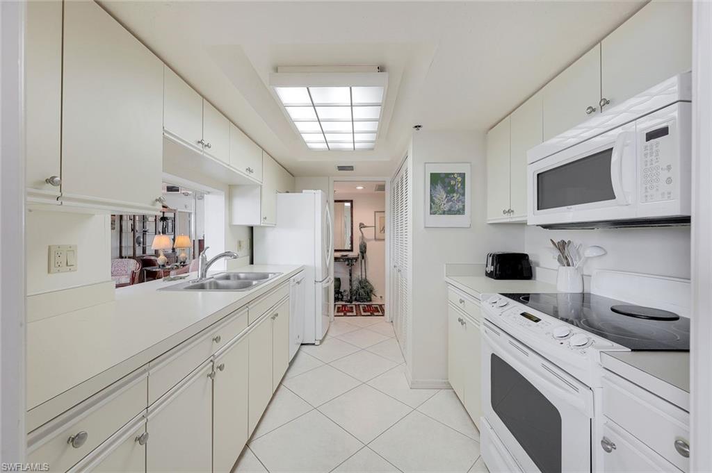 5501 Heron Point Drive, Unit 204 Naples, FL 34108 - Photo 7 of 23 a kitchen with a sink dishwasher stove and white cabinets