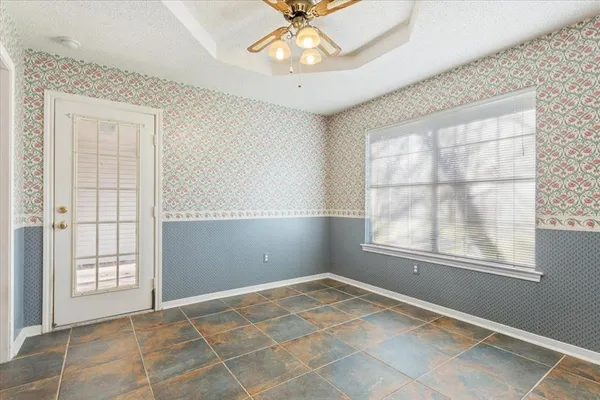 an empty room with chandelier fan and windows