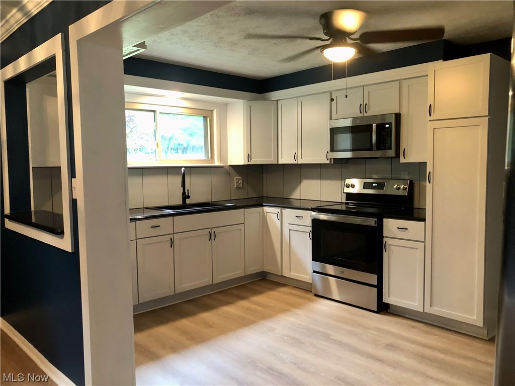 Kitchen with appliances with stainless steel 
finishes, dark countertops, white cabinets, backsplash, light vinyl floors, and ceiling fan