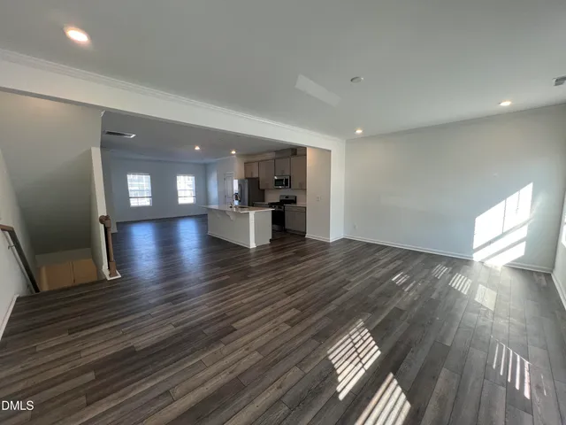 a view of empty room with wooden floor and kitchen