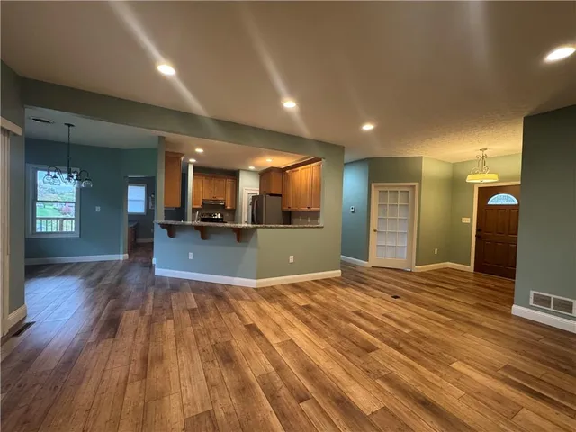 a view of an empty room with wooden floor and a kitchen