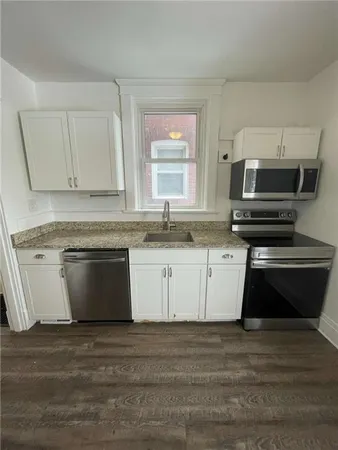 a white kitchen with granite countertop a stove and a sink