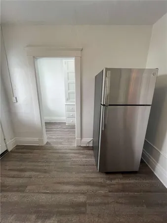 a view of a refrigerator in kitchen and an empty room with wooden floor