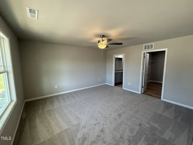 an empty room with chandelier fan and windows