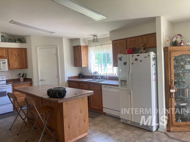 1095 County Road 70 Weiser, ID 83672 - Photo 10 of 44 Kitchen featuring wood cabinetry, tiled countertops, a central wood-finish island with a tiled surface, a window above the sink, and built-in overhead lighting