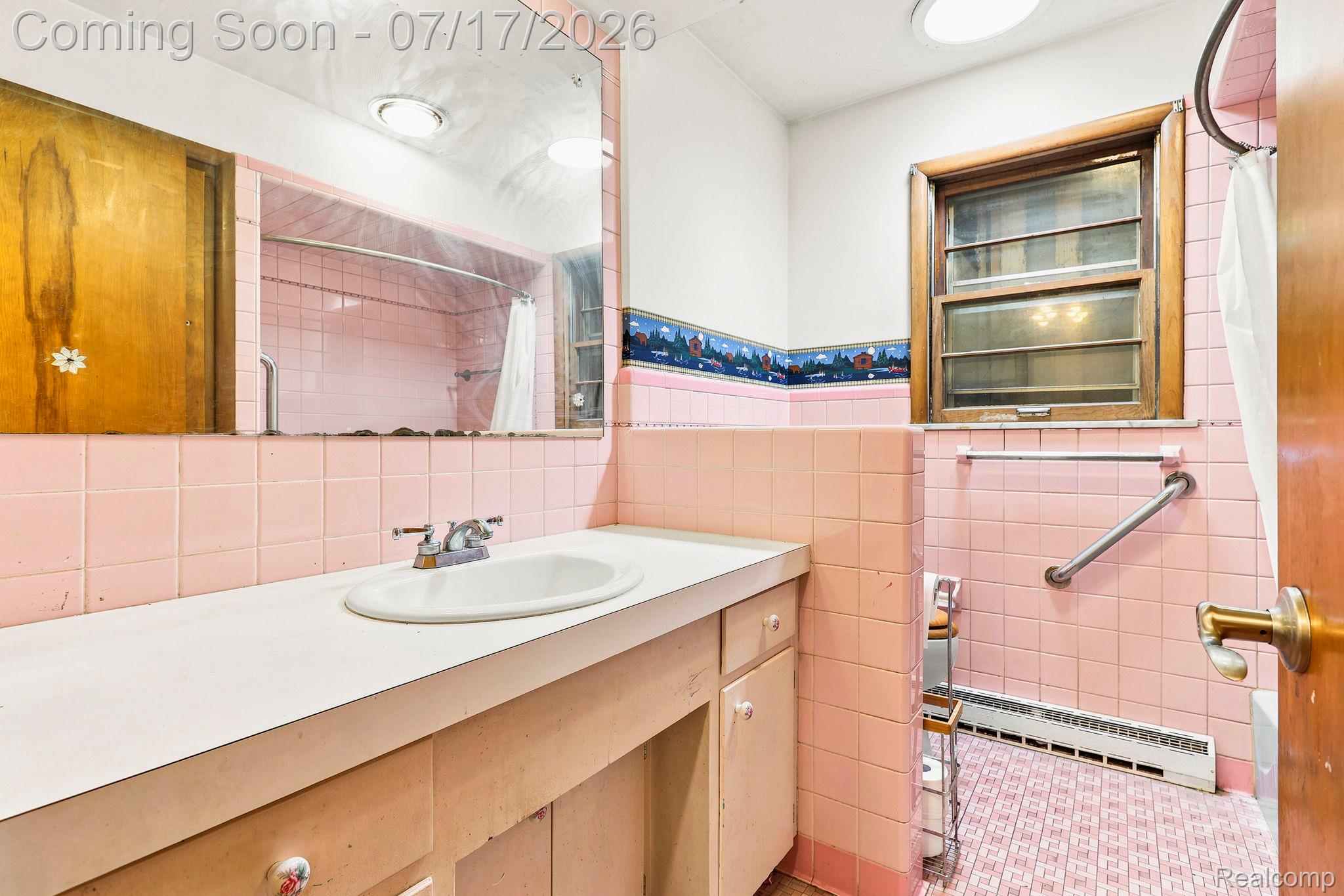 9805 Dolan Road Columbus, MI 48063 - Photo 14 of 39 Bathroom featuring a vanity with a white countertop and integrated sink, a large wall-mounted mirror, extensive pink tilework, a window with wood trim, and a grab bar