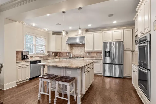 a kitchen with stainless steel appliances granite countertop a sink stove a refrigerator and white cabinets with wooden floor