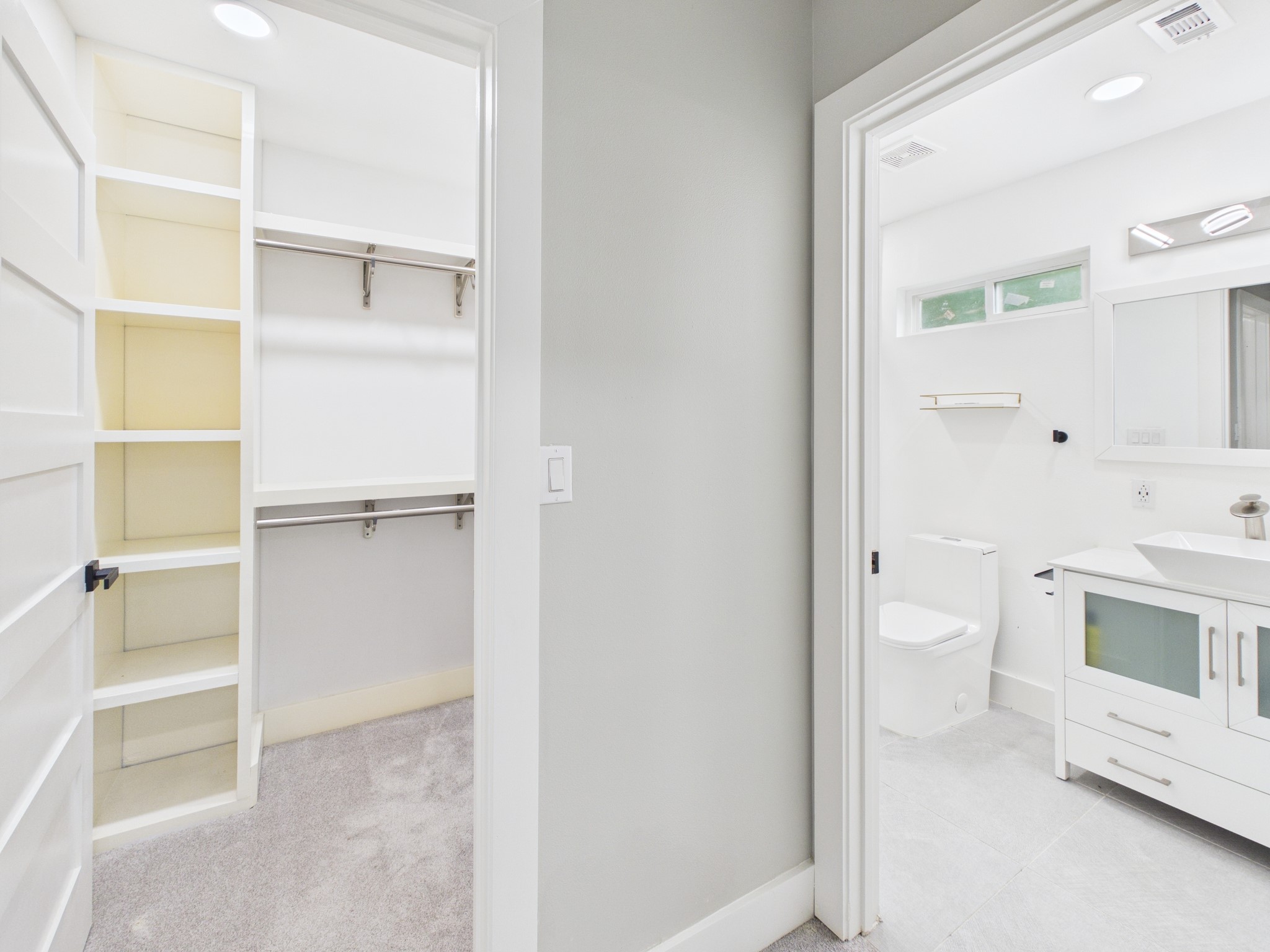 4927 Kelso Street Houston, TX 77021 - Photo 32 of 45 This photo features a modern bathroom and adjacent walk-in closet. The bathroom is well-lit with a sleek vanity, white fixtures, and a small window. The closet offers ample storage with shelving and hanging space, highlighted by clean, neutral tones.