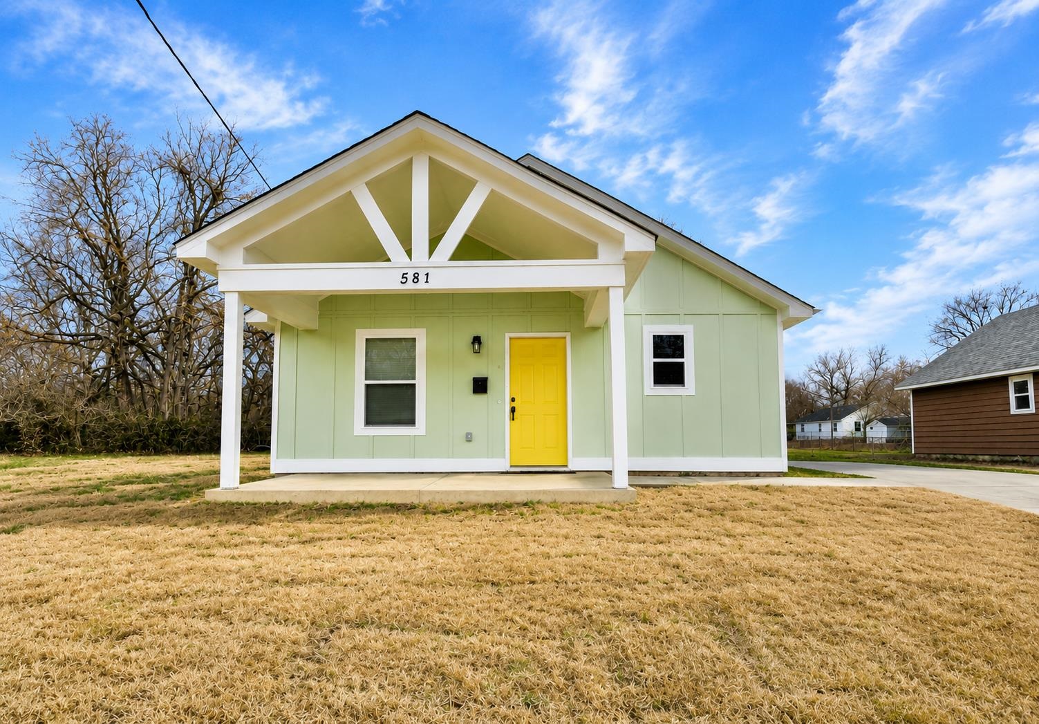 581 Gilleas Road Memphis, TN 38109 - Photo 1 of 1 Light green exterior siding, porch with white columns, white gabled entryway, yellow front door, and a paved driveway