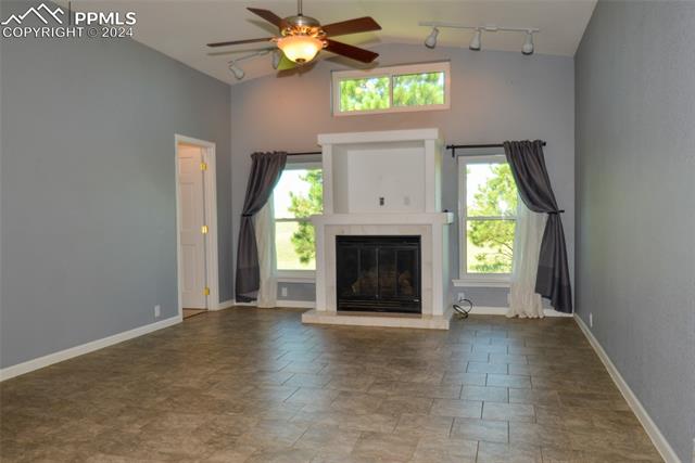 34115 Big Springs Road Yoder, CO 80864 - Photo 16 of 35 Unfurnished living room featuring a tiled fireplace, ceiling fan, track lighting, dark tile floors, and vaulted ceiling