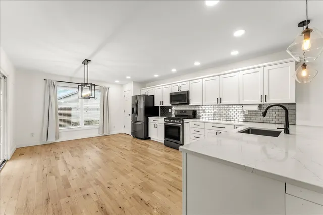 a large kitchen with kitchen island a stove a sink dishwasher a refrigerator and white cabinets with wooden floor