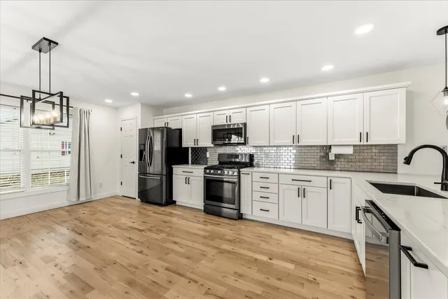 a kitchen with stainless steel appliances granite countertop a stove top oven a sink a refrigerator and white cabinets with wooden floor