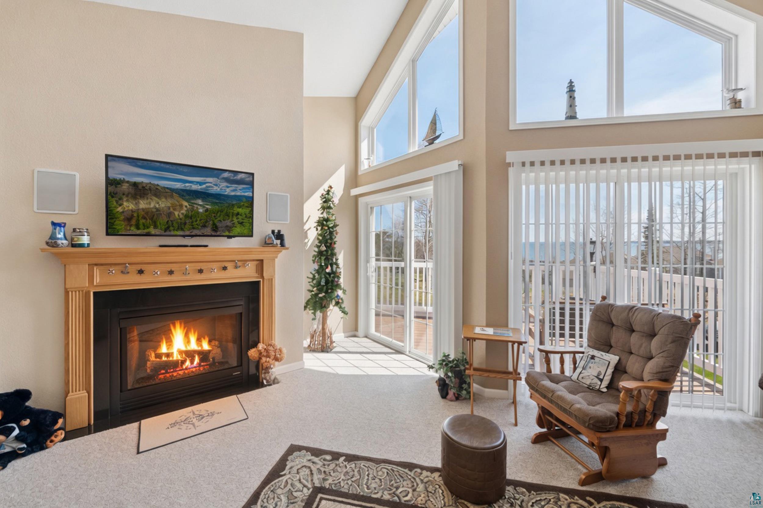 34590 Bay View Road, Unit 801 Bayfield, WI 54814 - Photo 8 of 36 Living room featuring a fireplace with a light wood mantel, high ceilings, large windows, and glass sliding doors leading to a balcony