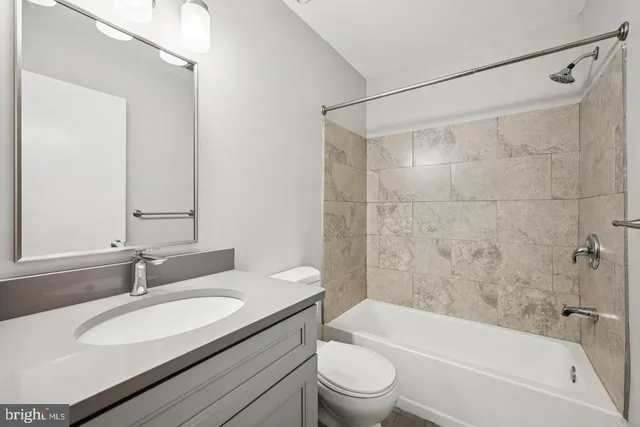 a bathroom with a granite countertop bathtub shower sink vanity mirror and toilet
