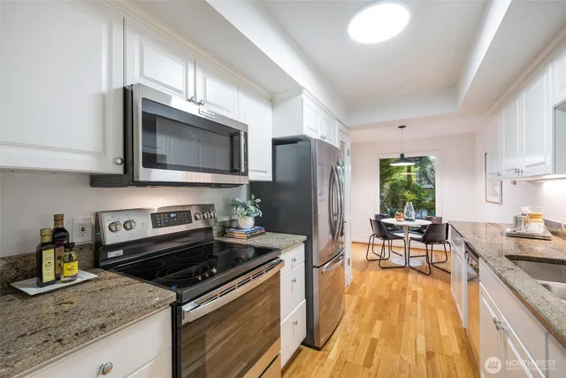 a kitchen with stainless steel appliances granite countertop a stove top oven a sink dishwasher a dining table and chairs with wooden floor