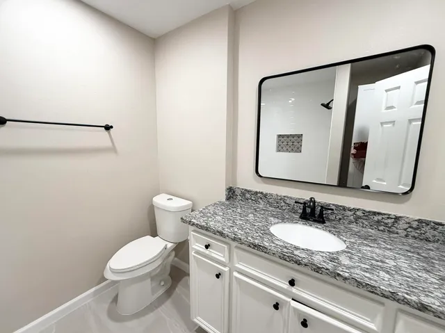 a bathroom with a granite countertop sink toilet and mirror